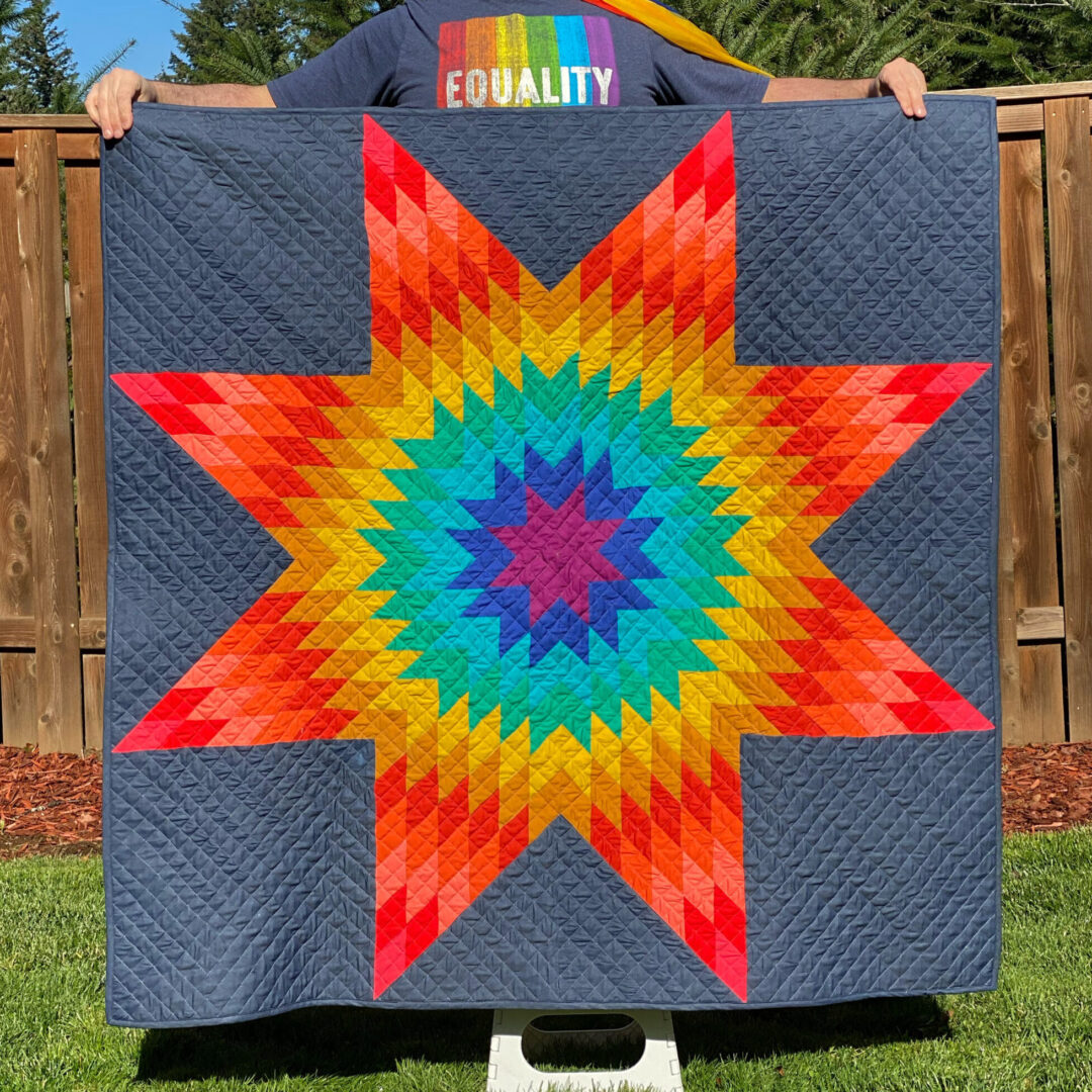 A man holding a Quilt with wooden fence behind