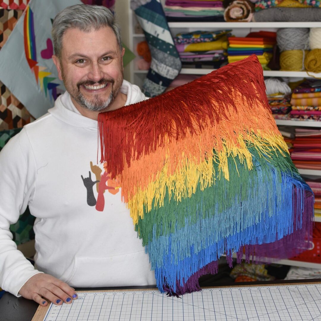 Mathew holding a fringed and rainbow-colored pillow case  