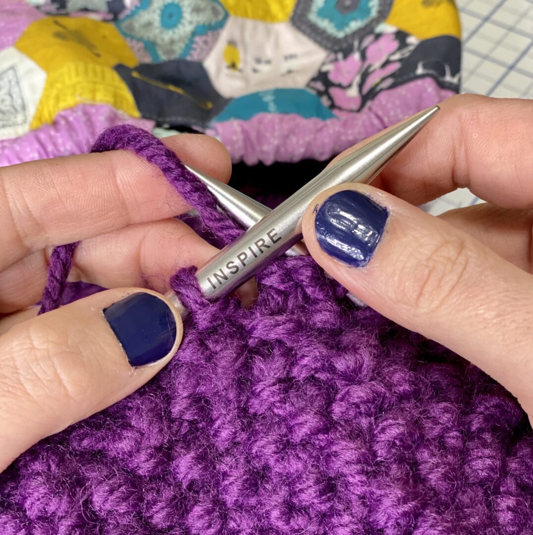 knitting a purple blanket with a pair of knitting needles