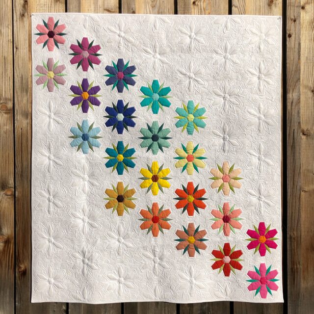 A colorful flower quilt hanging on a wooden wall